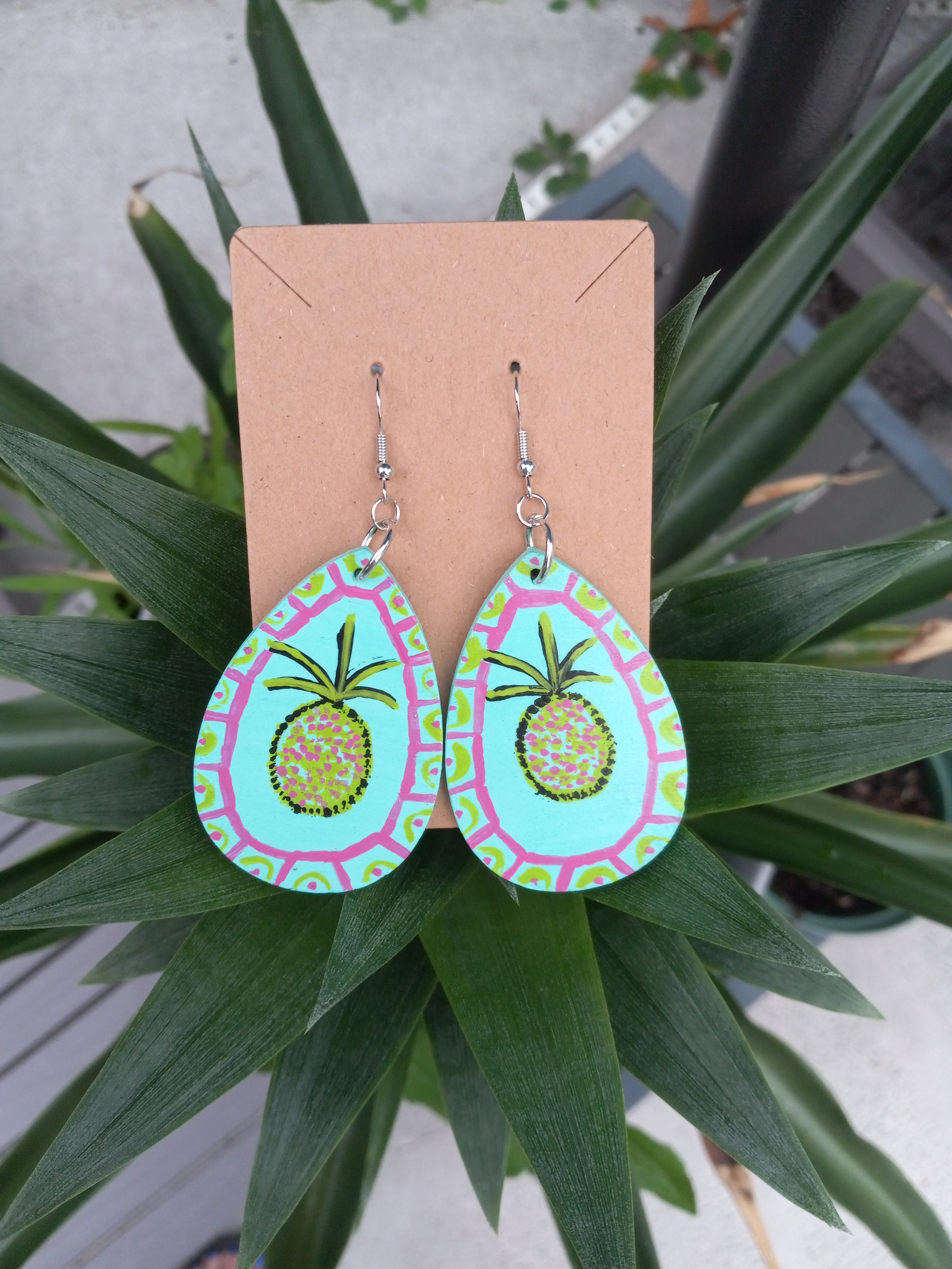 A pair of aqua blue teardrop shaped earrings with painted yellow pineapples in the center.